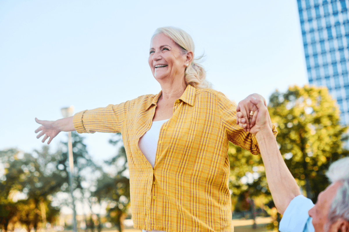 Happy senior mature couple having fun walking and balancing on a bench, bonding in a park outdoors.